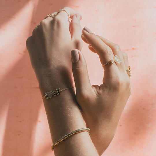 Kollektionsbild Schmuck_zwei Hände in einander verschlungen die Armbänder und Ringe Tragen vor einem rose Farbenen Hintergrund_TREND Kollektiv