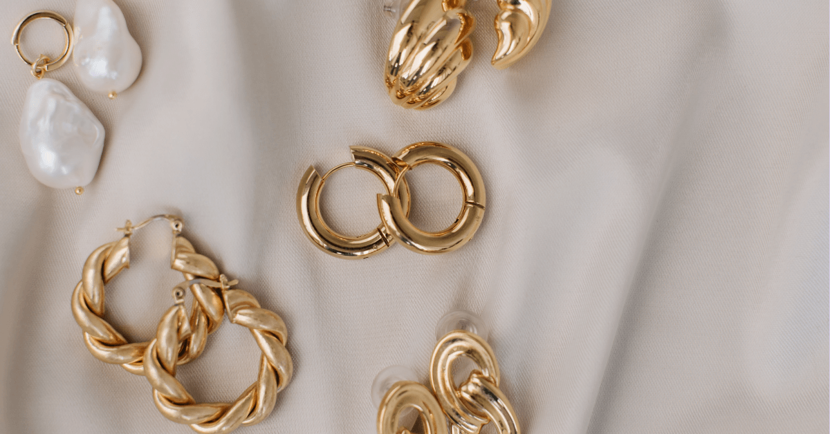 Goldene Statement-Ohrringe mit Perlen von TREND Kollektiv – stilvoll kombiniert auf edlem Stoffhintergrund