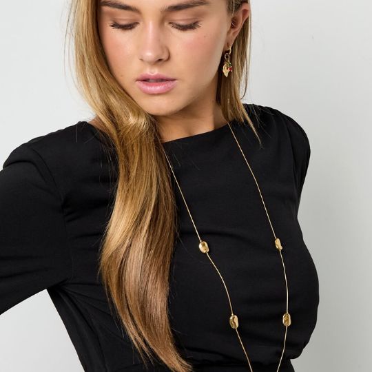 Blonde junge Frau trägt schwarzen Pullover und eine lange goldene Kette mit Goldnuggets um den Hals