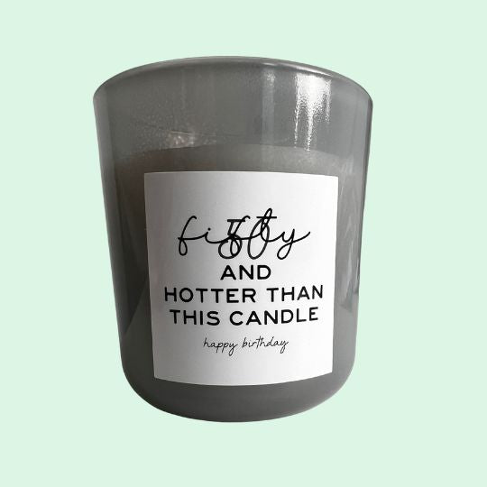 Graue Duftkerze im Glas mit der Aufschrift "fifty and hotter than this candle – happy birthday", stilvoller Geschenkartikel zum 50. Geburtstag