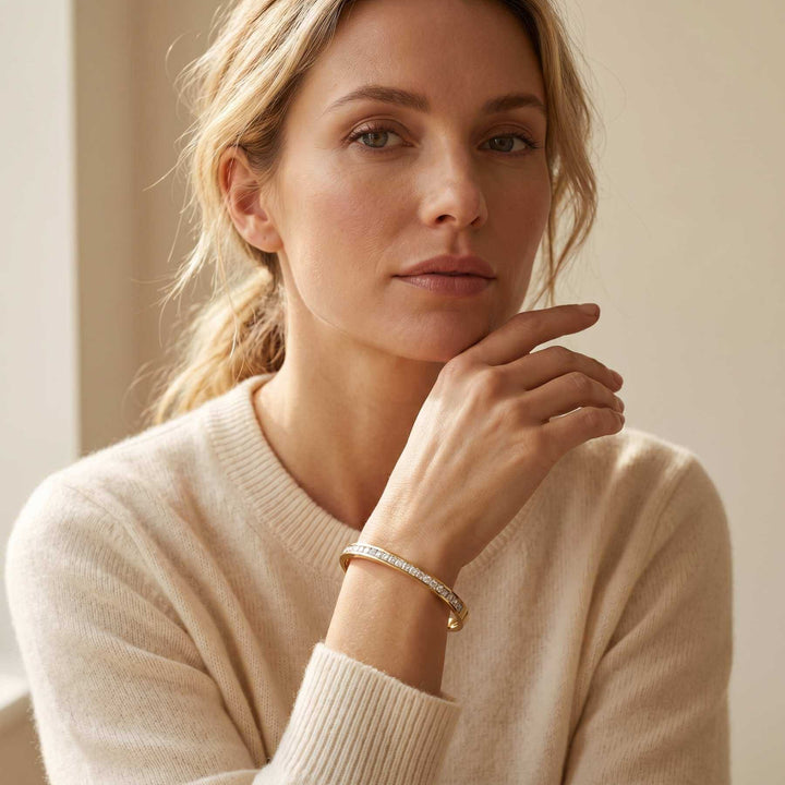 Eine reife blonde Frau in einem beigen Cashmere Pullover hält ihre Hand an das Kinn und man sieht das GRACE Bangke von TREND Kollektiv