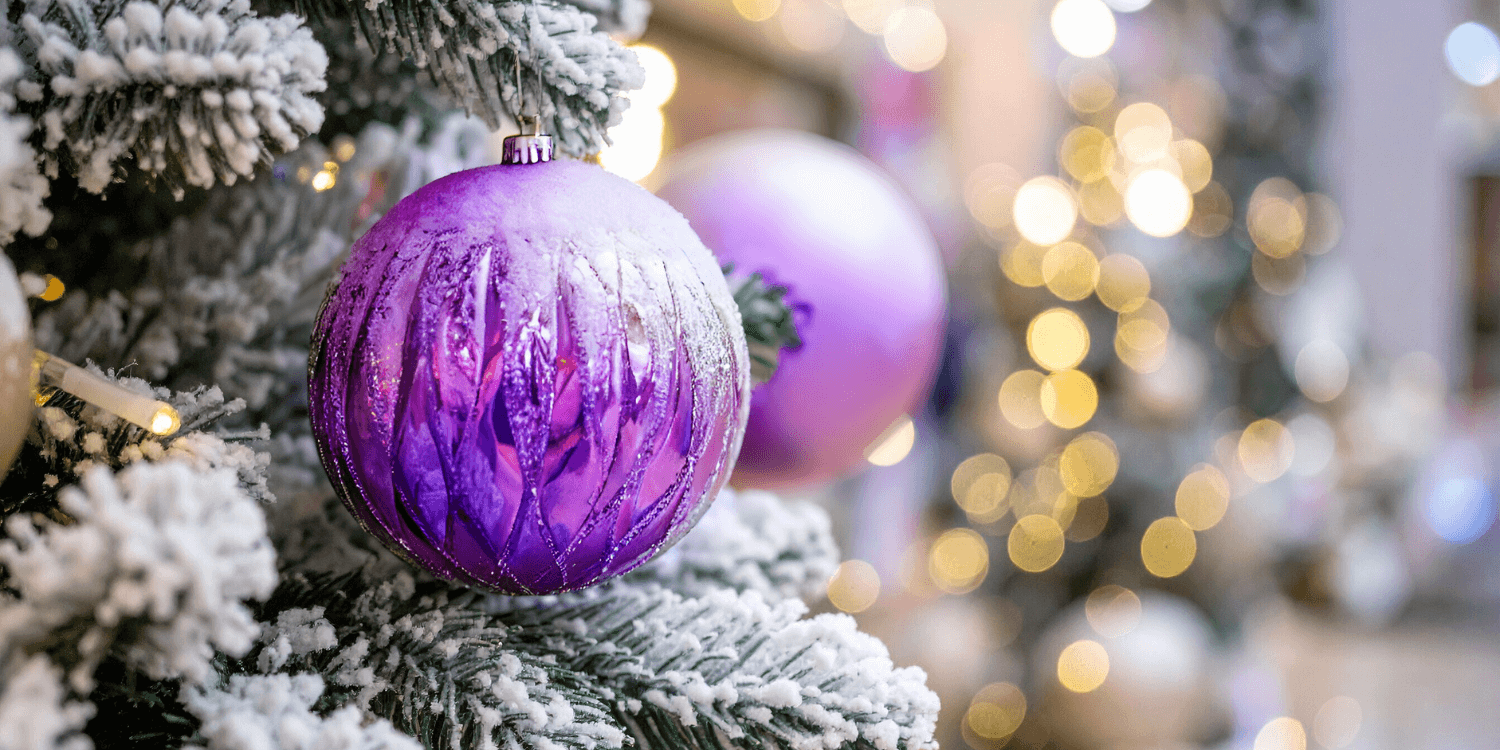 Man sieht einen Ausschnitt von einem mit Schnee bedeckten Weihnachtsbaum mit lila Baumkugeln-TReND Kollektiv
