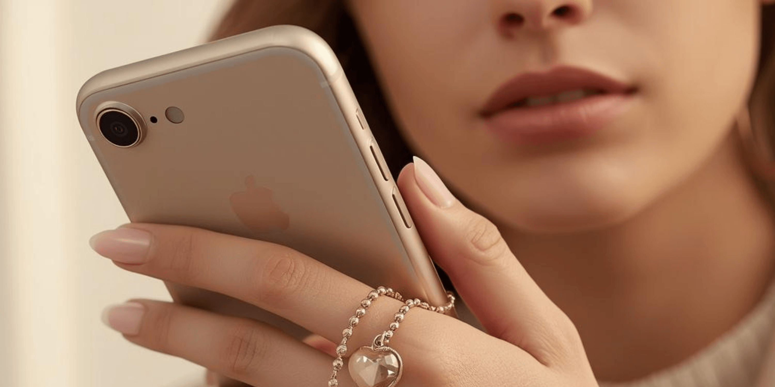 Im Auschnitt ist der Kopf einer Frau zu sehen die vor ihrem Gesicht ein Handy hält und eine Handykette noch über ihre Finger liegt. Farbwelt ist in beige Tönen. 