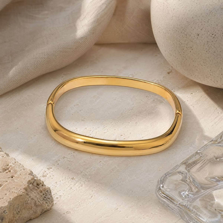 Noa Bangle in gold auf einem beigen Stein präsentiert als Moodbild von TREND Kollektiv