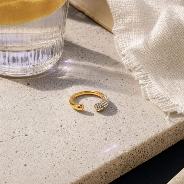 Sparkle Arc Ring inszeniert auf einem Stein Tisch mit Wasserglas - TREND Kollektiv – AI-GENERATED