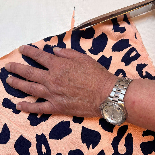 Hand einer älteren Schneiderin auf einem Leo Stoff, die ihn gerade zuschneidet. 