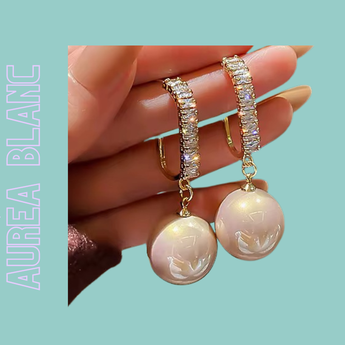 AURÉA Blanc – Elegante weiß-goldene Perlenohrringe mit Zirkonia-Steinen werden an den Händen gehalten von TREND Kollektiv