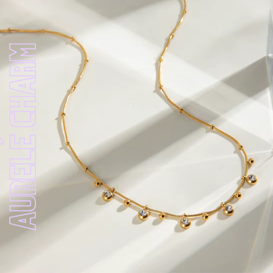 Zarte goldene Charm-Kette mit funkelnden Zirkonia-Tropfen gelegt auf einer hellen Oberfläche, 18k vergoldet, femininer Schmuck von TREND Kollektiv