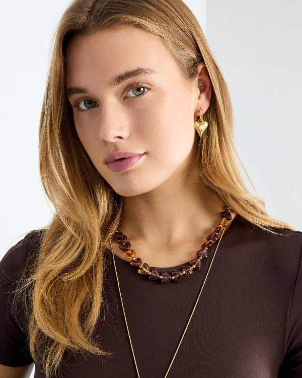HEART GLOW Kette mit herzförmigen Acryl-Perlen in Bernsteinoptik und goldfarbenem Edelstahl am Hals tragend– TREND Kollektiv