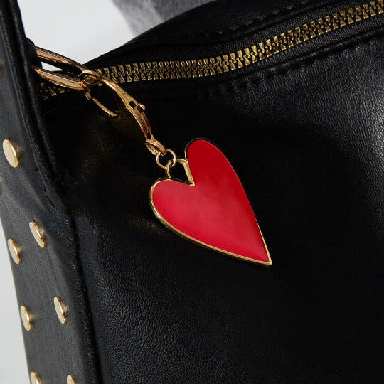 Bold Heart Charm Anhänger an einer schwarzen Tasche hängend. Das rote Herz aus Emaille mit goldenem Herzanhänger von TREND Kollektiv