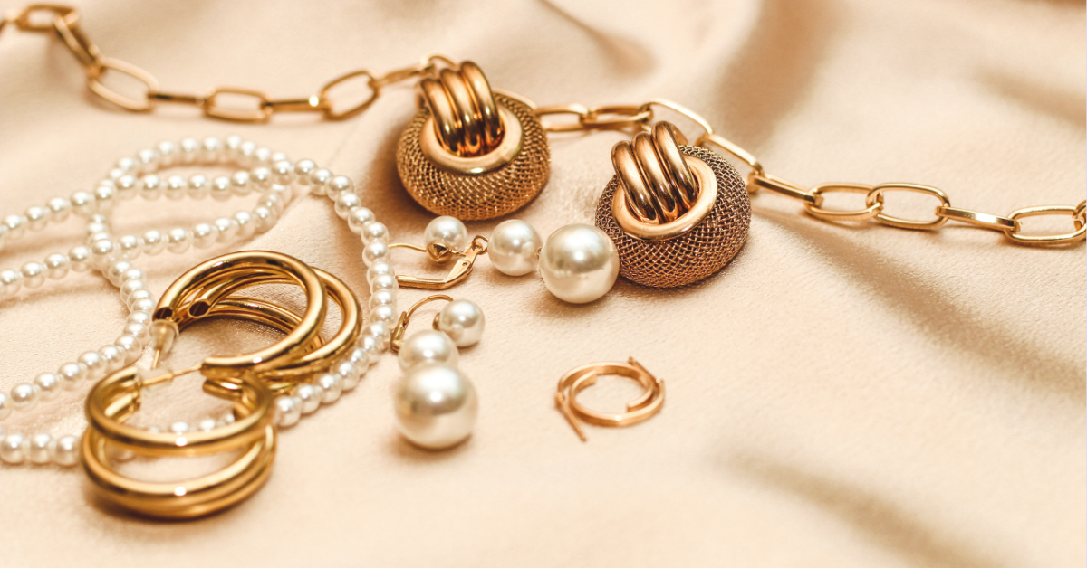 Stilvoll arrangierter Schmuck von TREND Kollektiv mit goldenen Creolen, Statement-Kette und Perlen auf beigem Stoff – moderner, femininer Look.